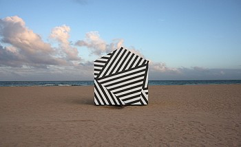 Photographic artwork titled Seascape 021412 (2013) by Max-Steven Grossman, a diasec-mounted satin print (Edition 1/5, 40 x 65 in.), featuring a black-and-white striped geometric structure on a sandy beach against the ocean and sky.